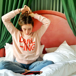 Darling Sweater by Castle. Girl sitting on bed twisting her hair